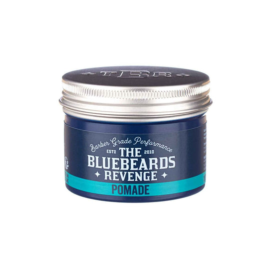 A container of hair pomade with a label that reads 'The Bluebeards Revenge Pomade'. The container is silver with a blue label and a orange cap.
