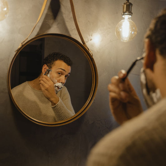 Black men wet shaving in front of mirror.