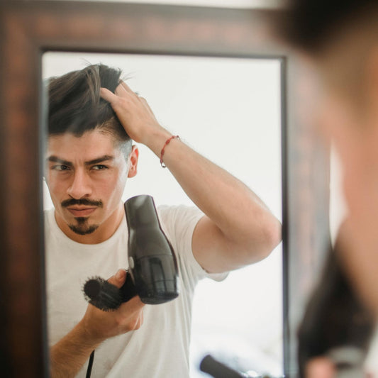 Man blow-drying his hair in front of a mirror.